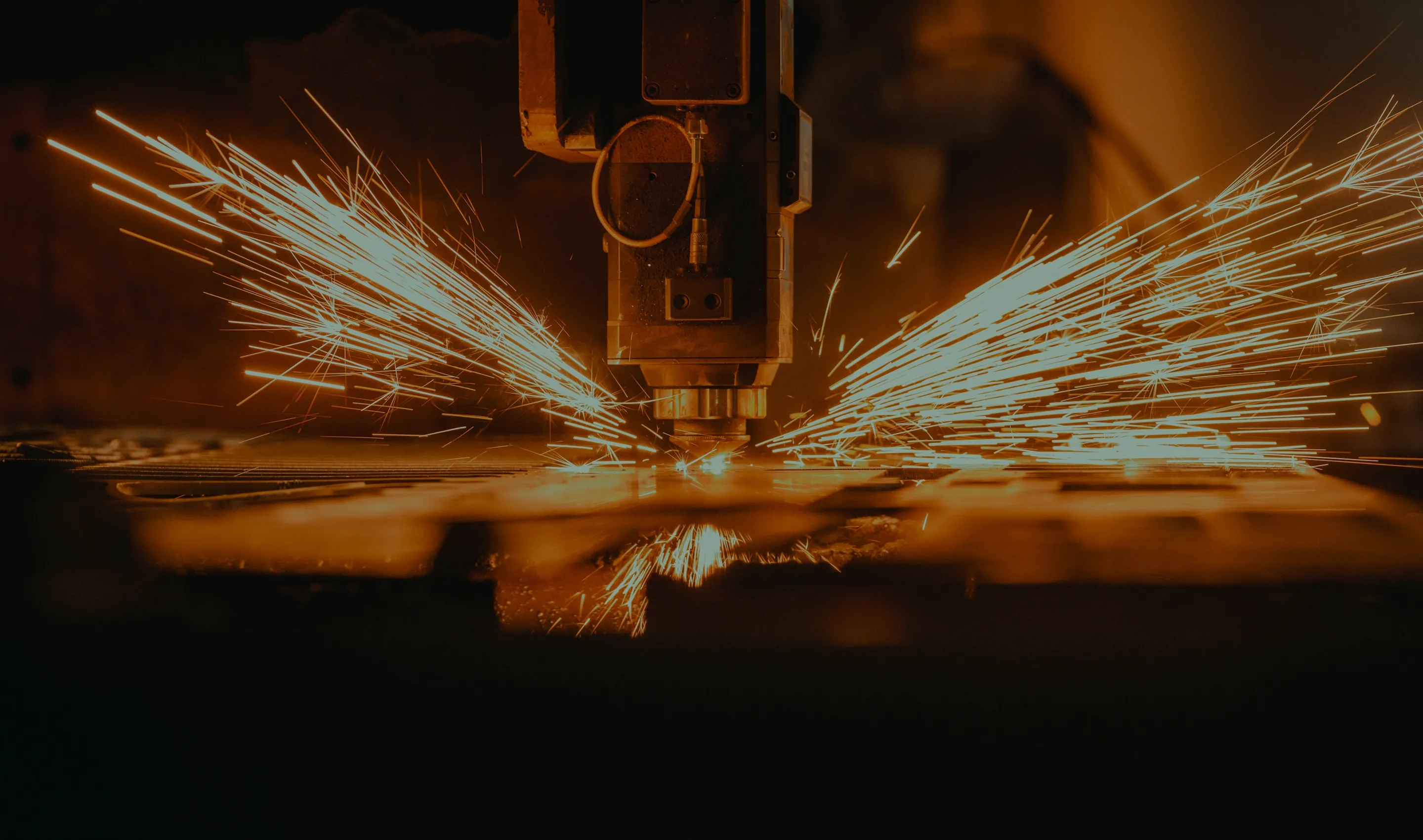 Close-up of a CNC laser cutting machine engraving metal with bright sparks flying outward from the cutting point.